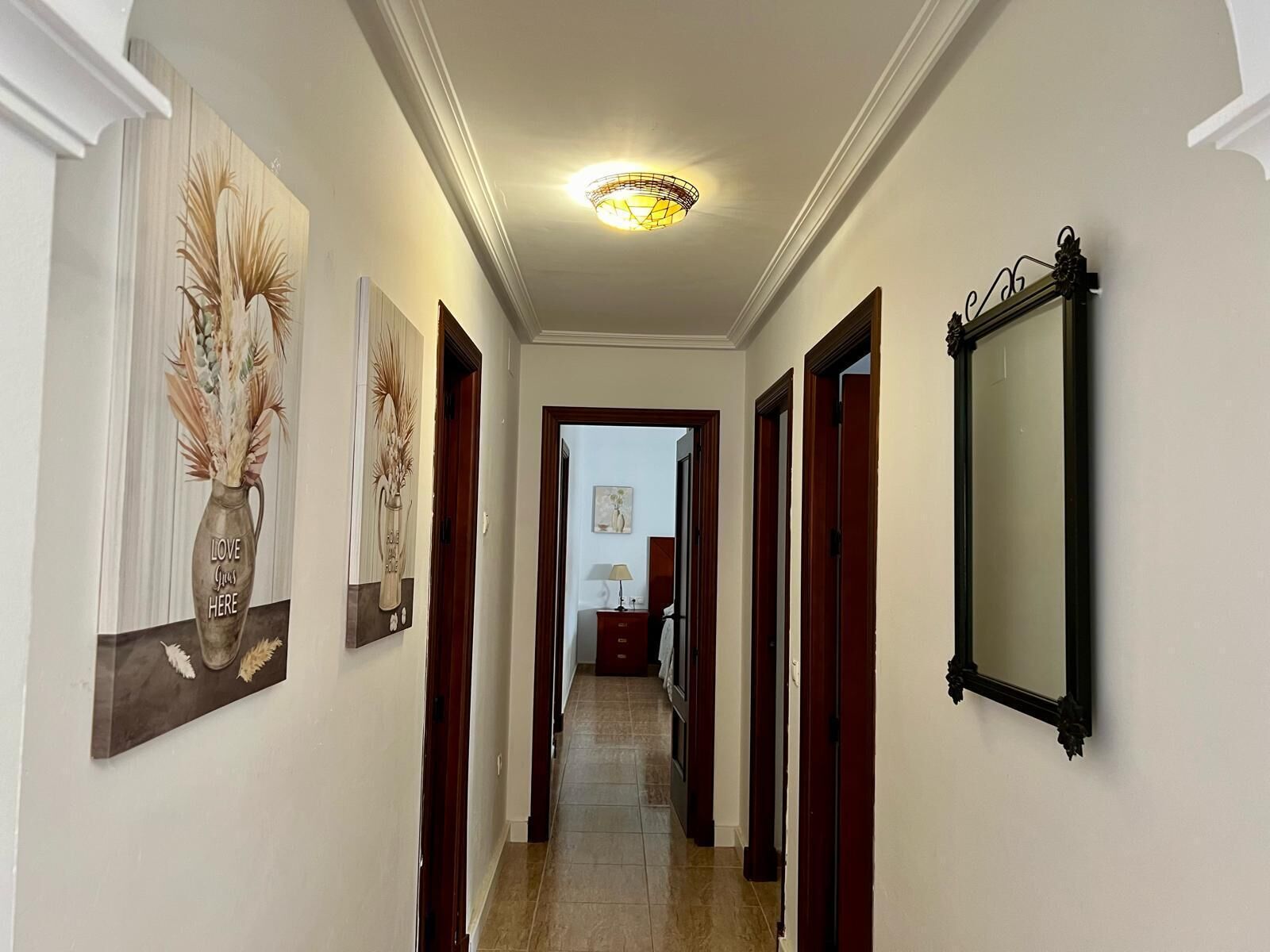 Un couloir avec un luminaire au plafond, des œuvres d’art encadrées accrochées aux murs et un miroir.