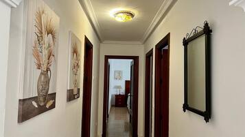 Un couloir avec un luminaire au plafond, des œuvres d’art encadrées accrochées aux murs et un miroir.