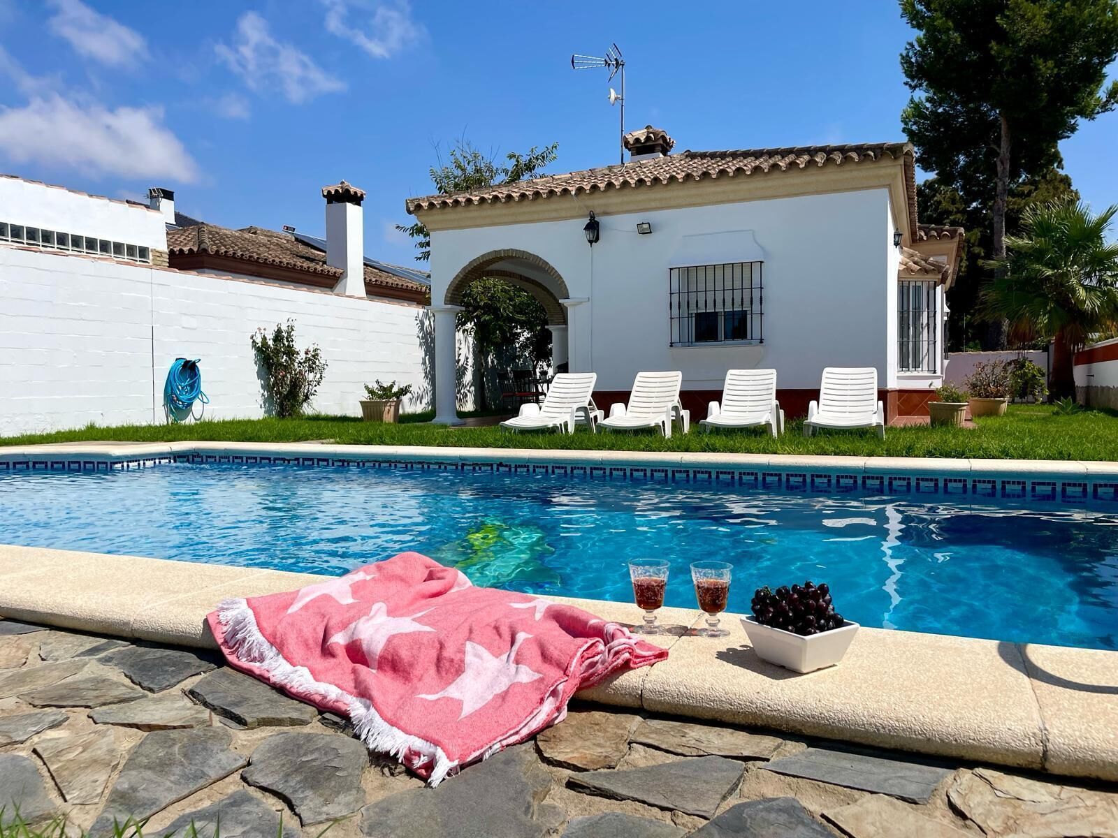 A swimming pool with lounge chairs, a white building with a tiled roof, and a clear blue sky.
