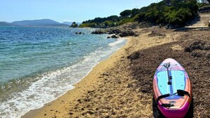 A beach with a surfboard on the sand, clear water, and a rocky shoreline. - Apartment in French Riviera with Pools (GRIMAUD)