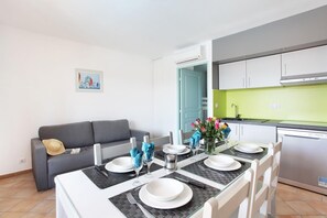 A dining area with a table set for four, a grey sofa, a kitchen with a green backsplash, and a framed picture on the wall.