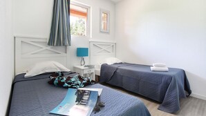 A bedroom with two beds, a nightstand, a window with curtains, and a magazine on the bed. - Apartment in Grimaud with Pools (GRIMAUD)