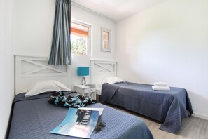 Ein Schlafzimmer mit zwei Betten, einem Nachttisch, einem Fenster mit Vorhängen und einer Zeitschrift auf dem Bett.