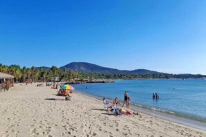 A beach with people sunbathing, a clear sky, and a mountain in the background.