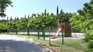 A playground with a red slide and climbing wall, surrounded by trees and a fence. - Apartment in Grimaud with Pools (GRIMAUD)