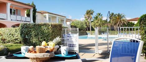A poolside table with food and drinks, a chair, and a sign indicating a surveillance area.