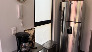 A kitchen with a stainless steel refrigerator, a coffee maker, a small trash bin, and a decorative plate on the wall. - Department in the Heart of Oaxaca (Oaxaca)