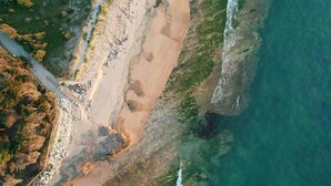 Eine Küstenlandschaft mit Sandstrand, steinigen Klippen und freiem Blick auf den Ozean.