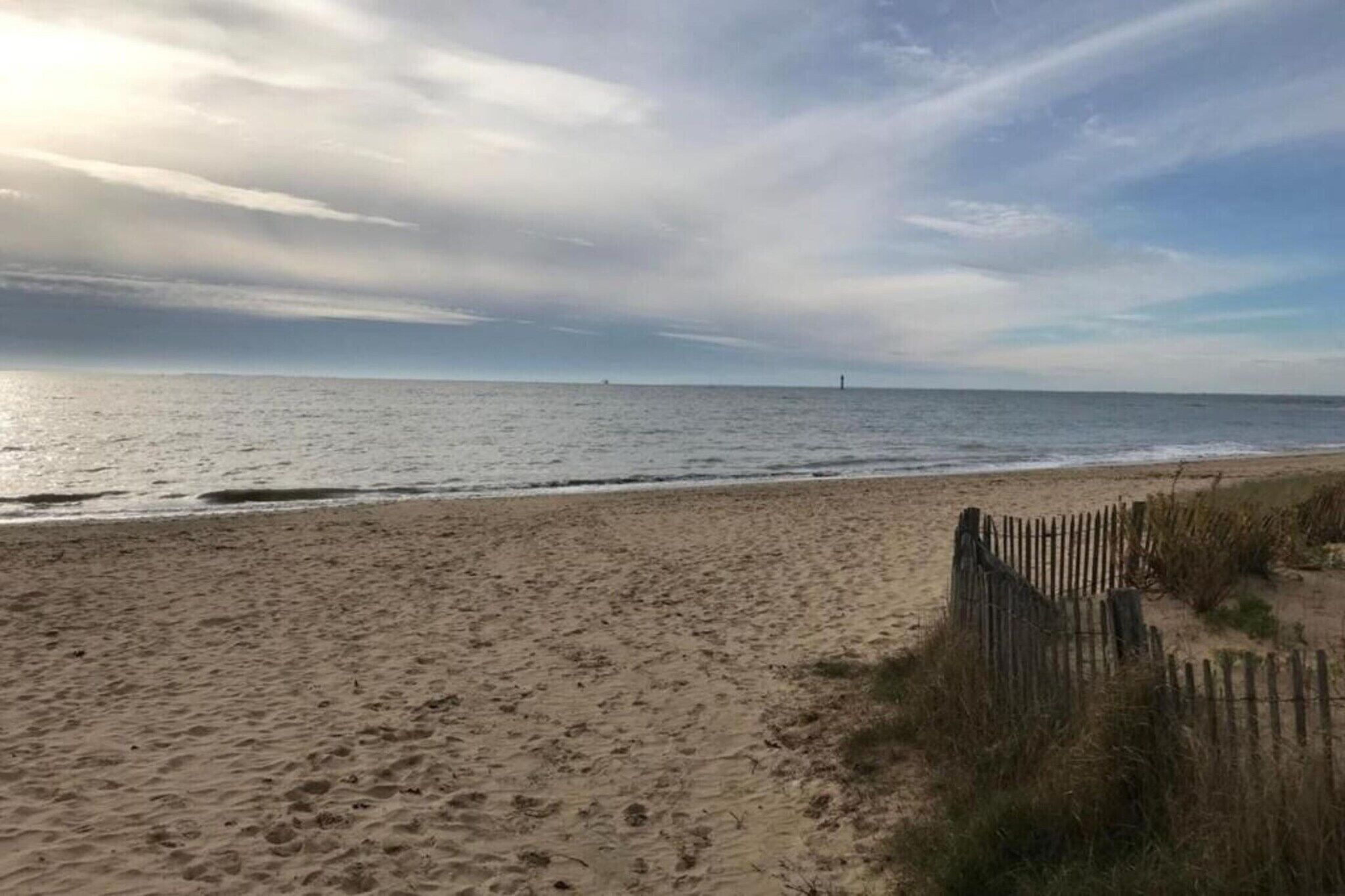 A beach with a wooden fence and a lighthouse in the distance.