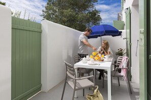 An outdoor dining area with a table, chairs, and a blue umbrella. - Nice apartment on the island of Ile de Ré (RIVEDOUX PLAGE)