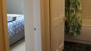 Een badkamer met douchegordijn met een tropisch bladpatroon, een witte deur en een betegelde vloer.