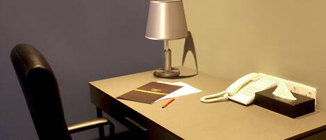 A small office space with a desk, chair, lamp, telephone, and a trash bin.
