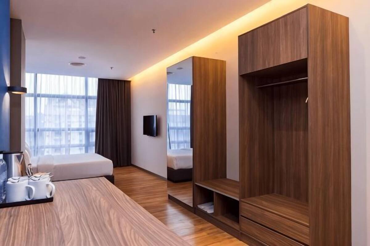 A modern hotel room with a wooden floor, a bed, a TV, a wardrobe, and a window with curtains.