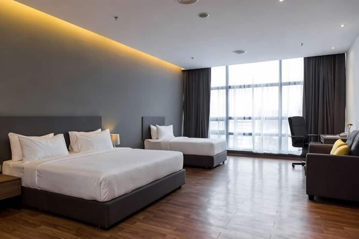 A hotel room with two beds, a sofa, a desk, and large windows.