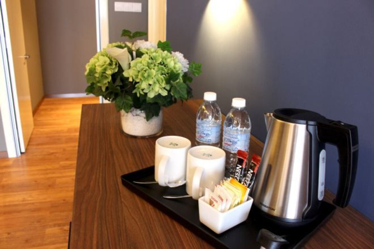 Una bandeja con dos tazas blancas, dos botellas de agua, una tetera eléctrica negra y un pequeño recipiente con bolsitas de té sobre una mesa de madera.