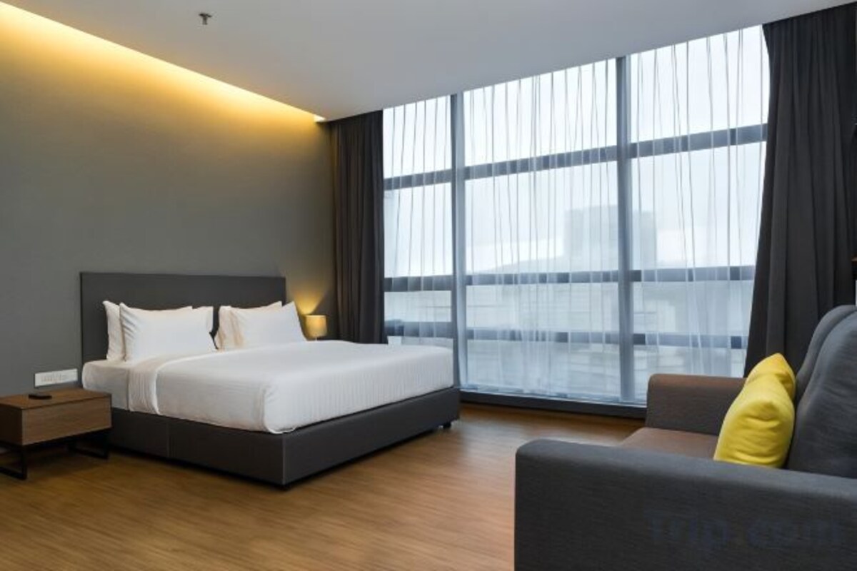 Una camera d'albergo moderna con un letto grande, un divano e un'ampia finestra con tende.