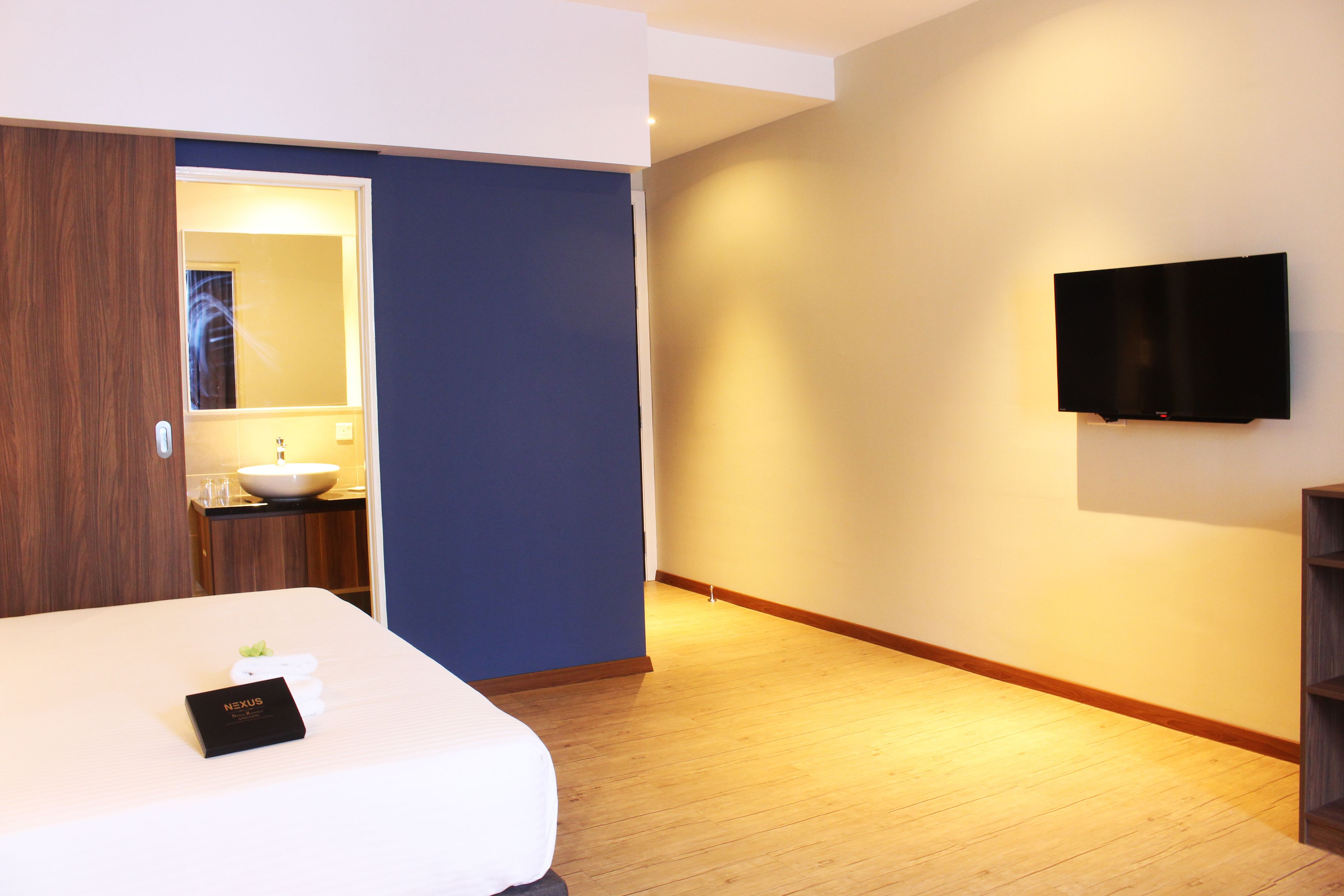 A hotel room with a bed, a bedside table, a mirror, a TV mounted on the wall, and a wooden floor.
