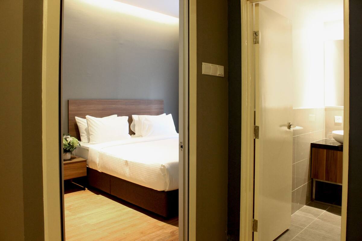 A hotel room with a bed, bedside table, and a bathroom with a sink and mirror.