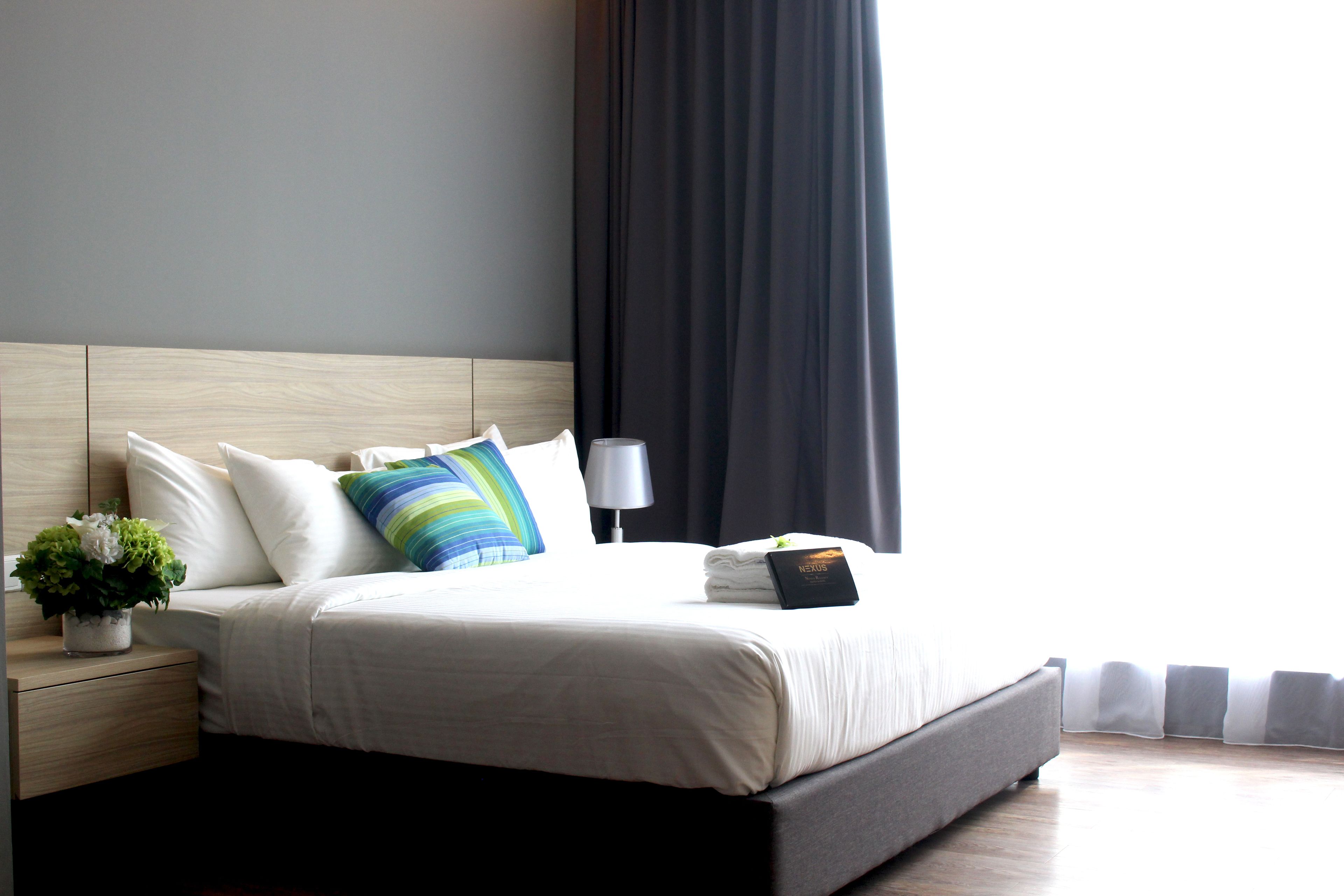 A neatly made bed with a white comforter, a striped pillow, and a small potted plant on the nightstand.