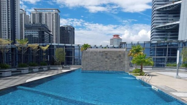 A swimming pool with a stone wall in the center, surrounded by a cityscape with modern buildings.