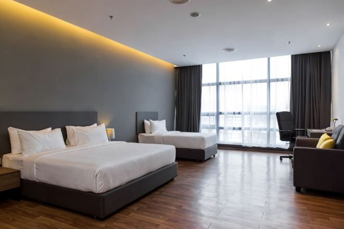 Habitación de hotel con dos camas, un sofá, un escritorio y ventanas amplias.