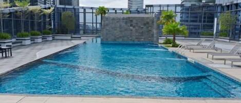 A rooftop pool with clear blue water, surrounded by modern buildings and palm trees.