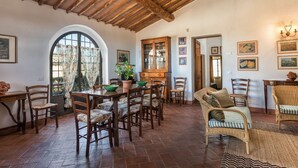 A dining area with wooden furniture, a large window with curtains, and a rustic ceiling. - Apartment with A/C, WIFI, pool, TV, patio, pets allowed, panoramic view, close to Greve In Chianti (San Donato)
