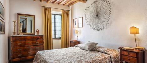 Un dormitorio con techo de madera, una cama con ropa de cama estampada, una mesita de noche, un aparador y una decoración en la pared.