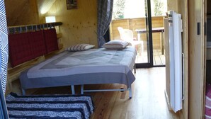 Un interior de madera con una cama, un banco y una puerta corrediza que da a un espacio exterior.