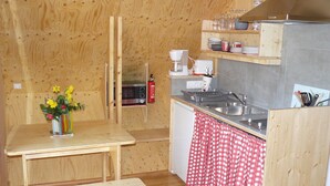 Cocina compacta con paredes de madera, microondas, cafetera y un lavamanos.