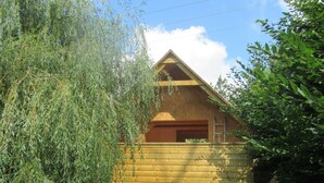 Una cabaña de madera con techo inclinado, rodeada de abundante vegetación y un cielo despejado.
