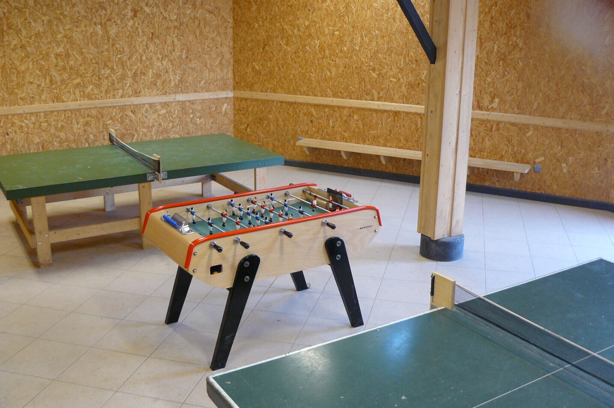 A foosball table with a green table and two benches, set against a wooden wall.