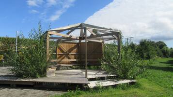 A wooden structure with a metal frame, surrounded by greenery and a clear sky.