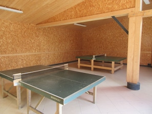 Une pièce avec deux tables de ping-pong, des murs en bois et un plafond en pente.