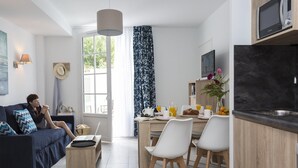 Ein modernes Wohnzimmer mit einer Couch, einer Essecke mit Stühlen, einer Küche inklusive Mikrowelle und einem großen Fenster.
