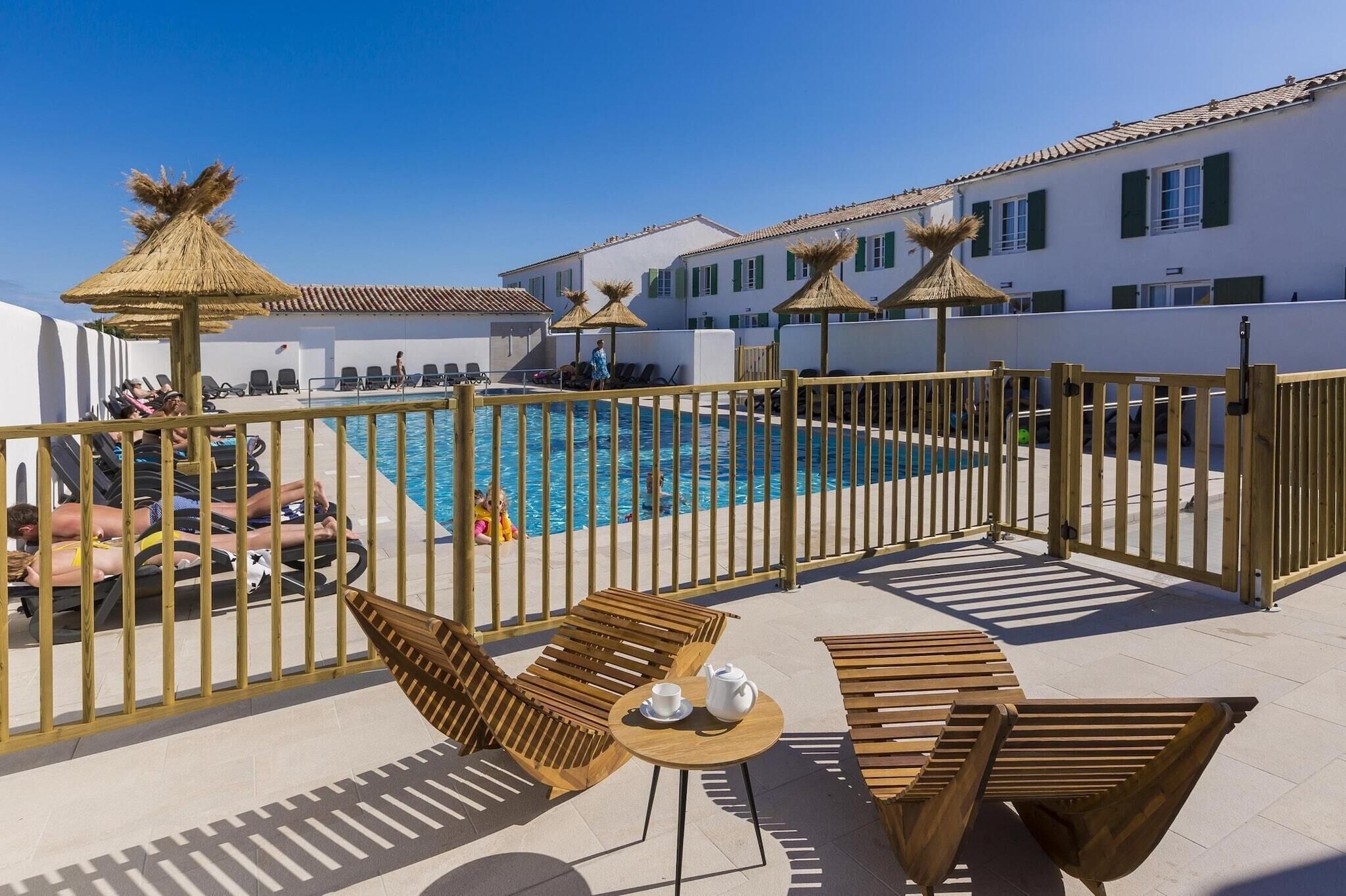 Un espace aménagé au bord de la piscine, avec des meubles en bois et des parasols, donnant sur une piscine.