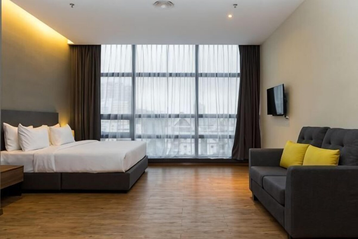 A hotel room with a bed, a sofa, a TV, and a large window with curtains.