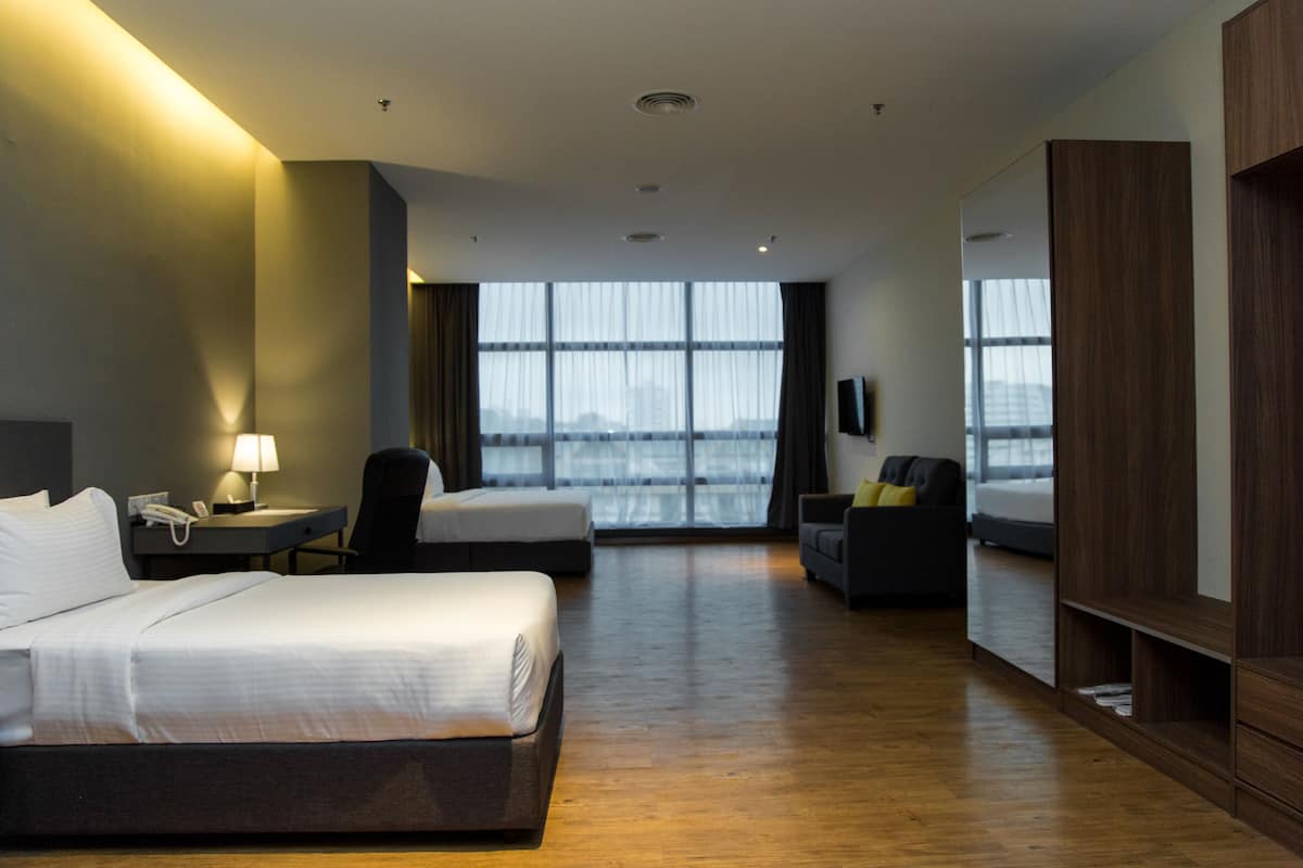 Habitación de hotel con una cama grande, un escritorio con lámpara, una silla, un sofá y una televisión. Amplias ventanas con cortinas.