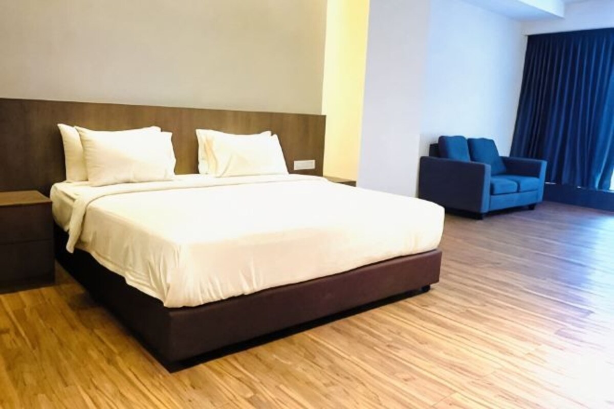 Habitación de hotel con una cama grande, mesita de noche, sofá y vistas al exterior.