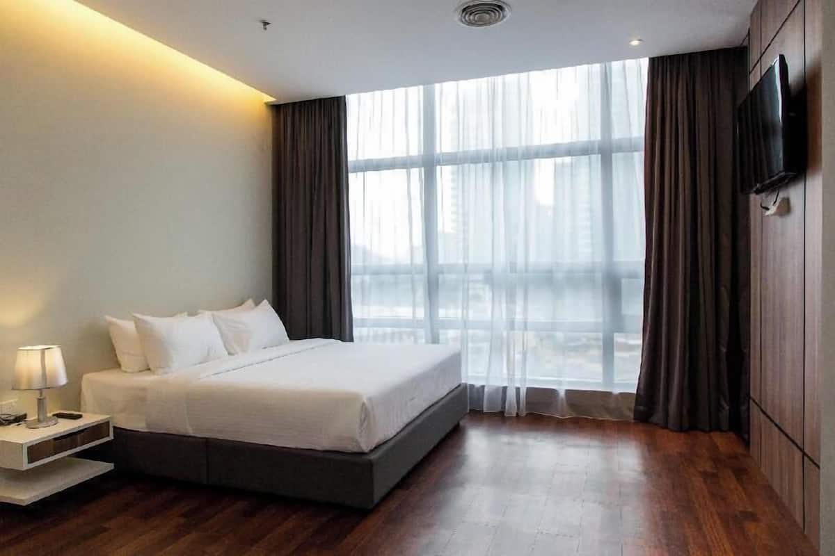 Habitación de hotel con cama, mesita de noche, televisor y un amplio ventanal con cortinas.