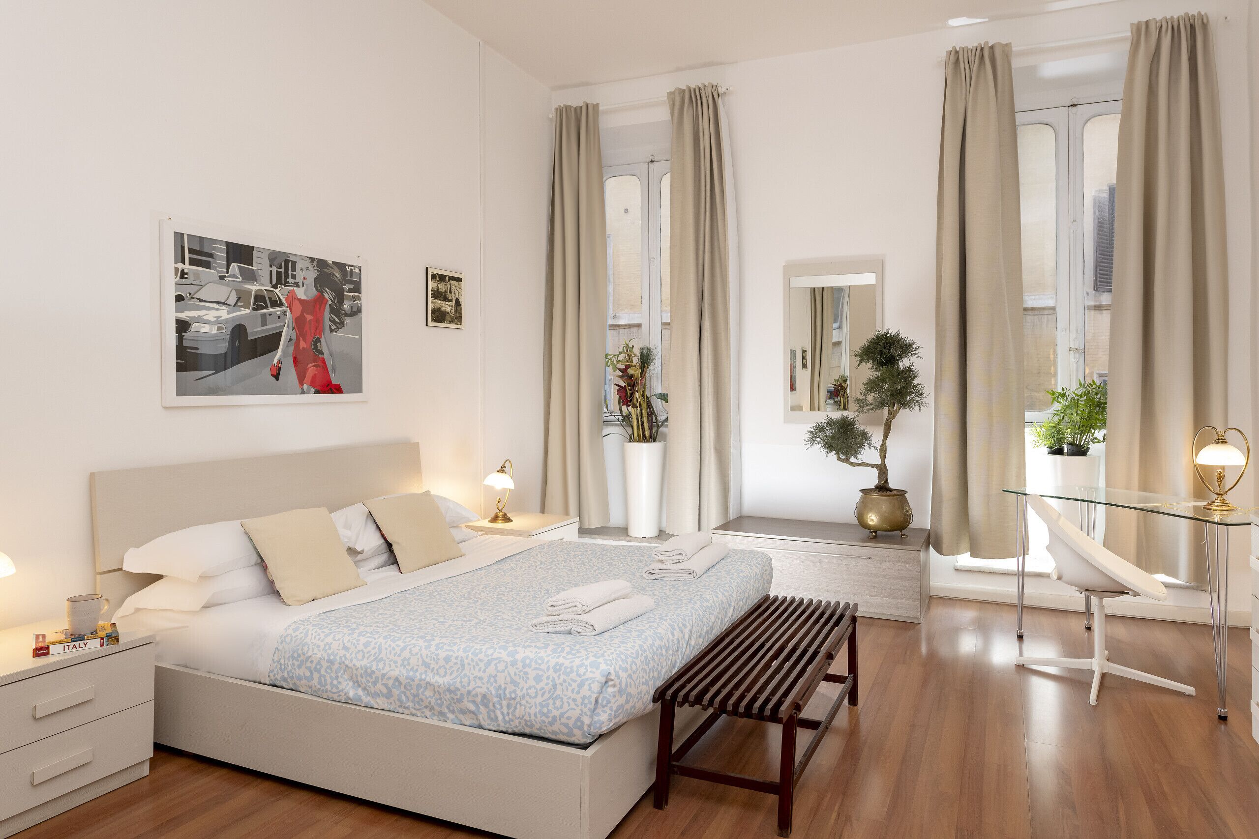 A modern bedroom with a bed, bedside tables, a desk, and a window with curtains.