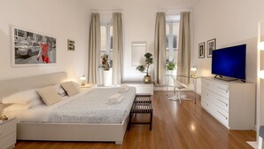 A modern bedroom with a bed, bedside tables, a TV, and a desk with drawers.