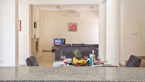 Een moderne woonkamer met een grijze bank, een flatscreen televisie en een eethoek met een granieten aanrecht, eettafel en stoelen.
