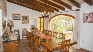 Zona pranzo con tavolo in legno apparecchiato per sei persone, circondato da sedie, con un lampadario sopra e vista sul verde attraverso una finestra ad arco.