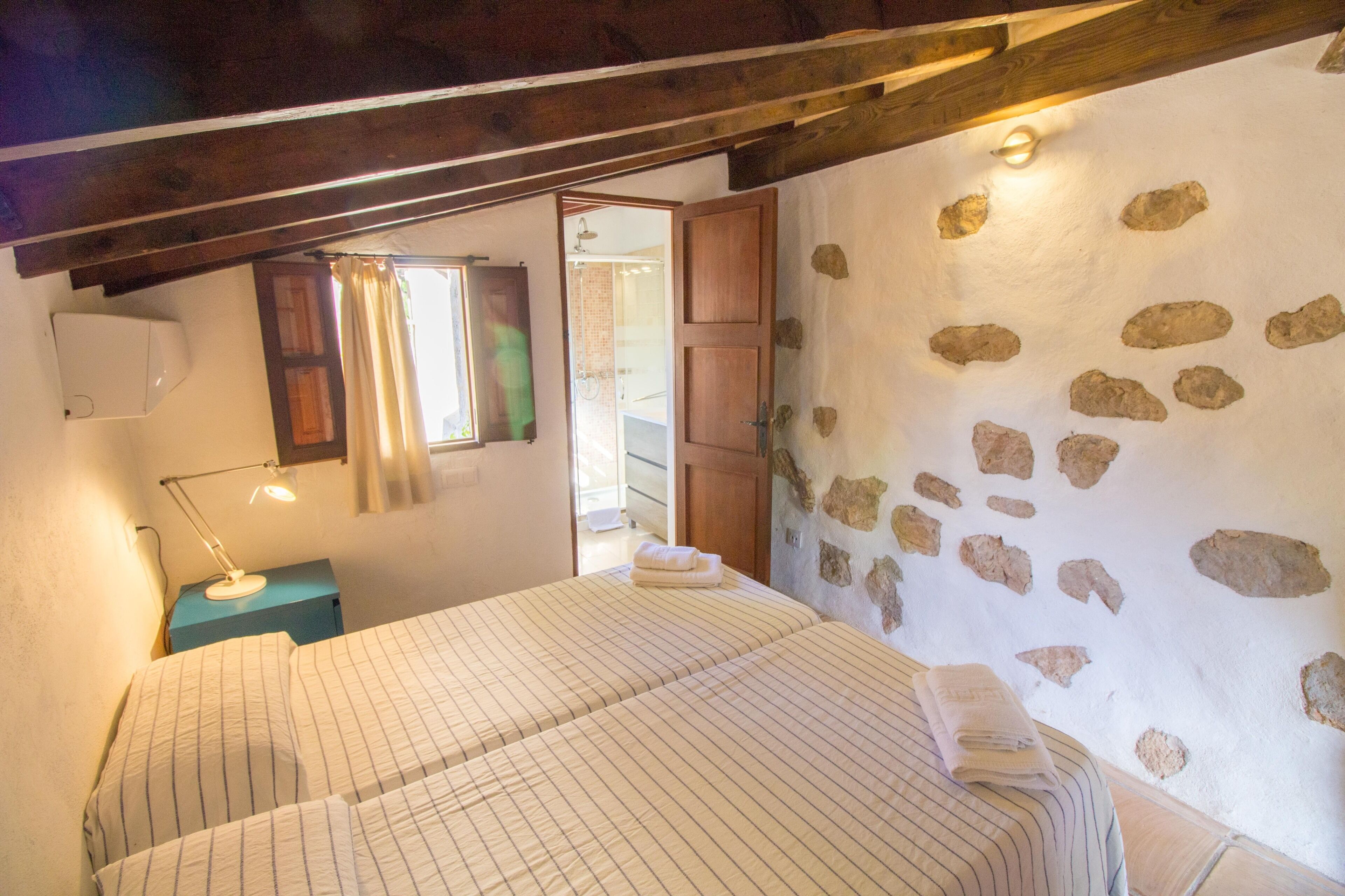 Un dormitorio con una cama, una mesita de noche, una lámpara, una ventana con cortinas y una pared de piedra.