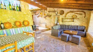 Un interno rustico con pareti in pietra, un tavolo di legno con tovaglia fantasia, mobili in vimini e diverse bottiglie su uno scaffale.