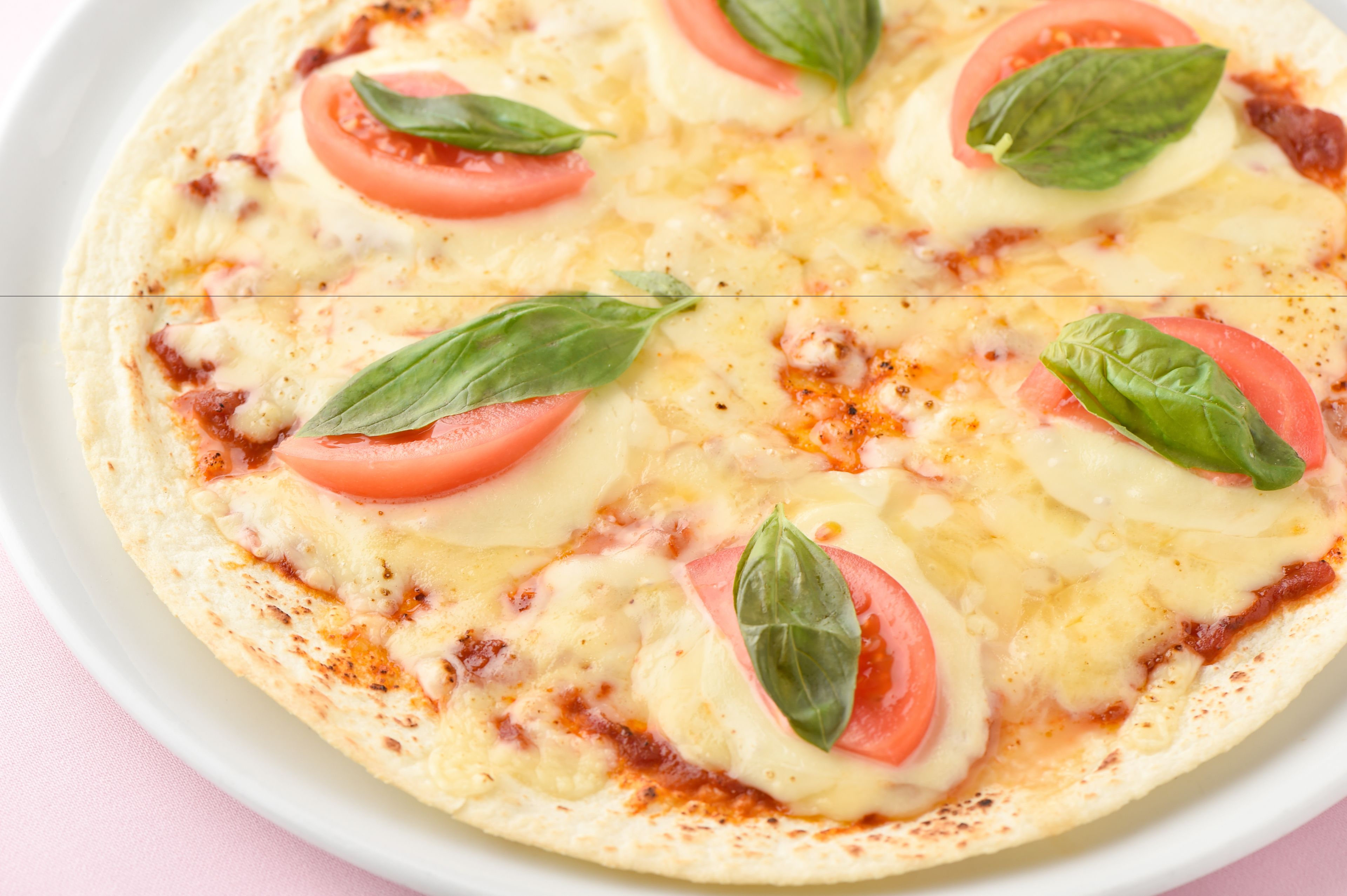 A pizza with tomato slices and basil leaves on a white plate.