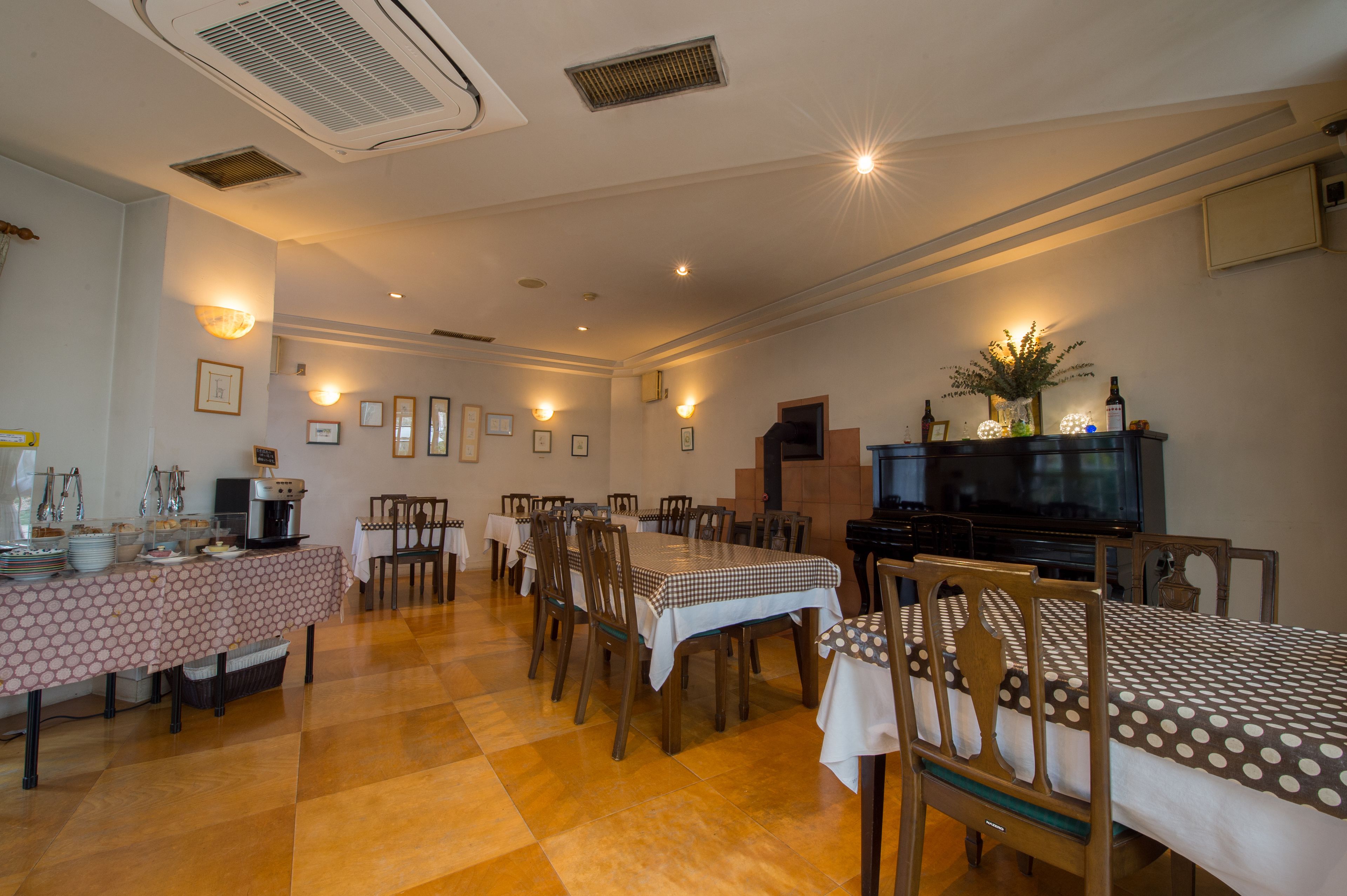 Comedor con varias mesas y sillas, una estación de café y un televisor sobre un soporte.