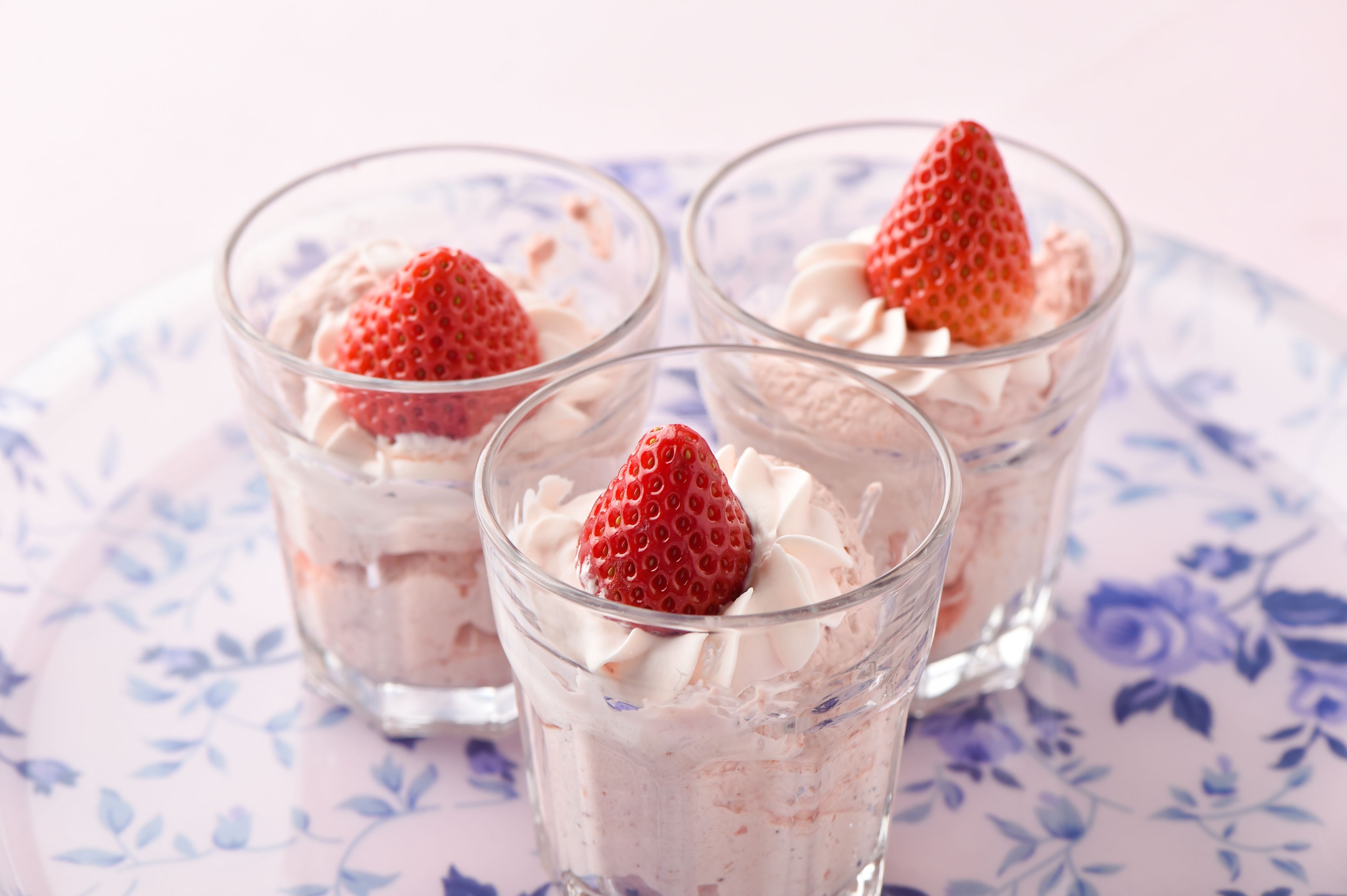 Three glasses of dessert with strawberries on a floral plate.