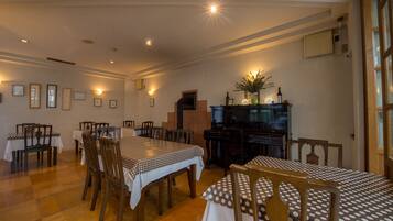 A dining area with multiple tables and chairs, a piano, and wall-mounted lights.